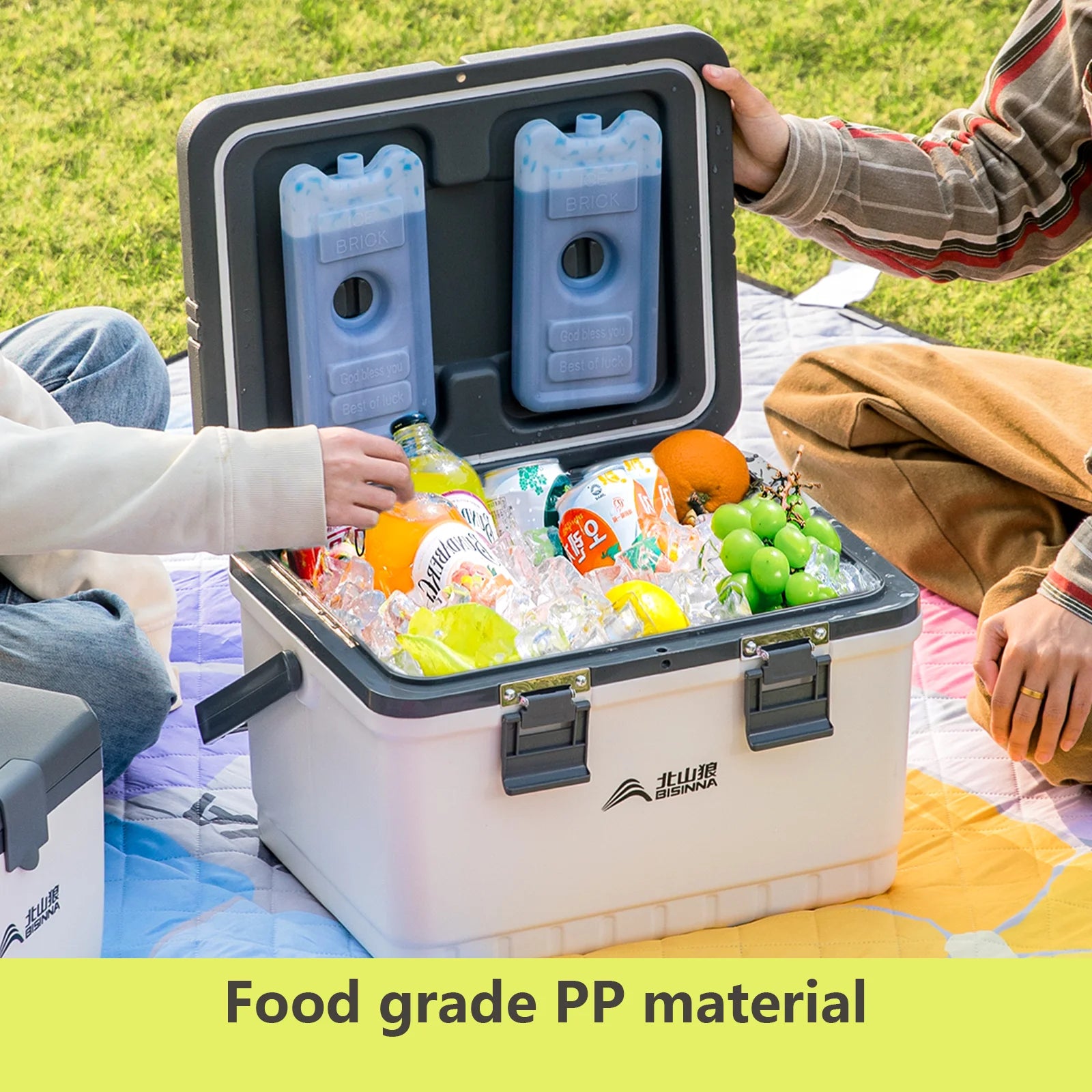 People opening a BISINNA cooler box filled with drinks and fruits on a grassy area, with 'Food grade PP material' text at the bottom.