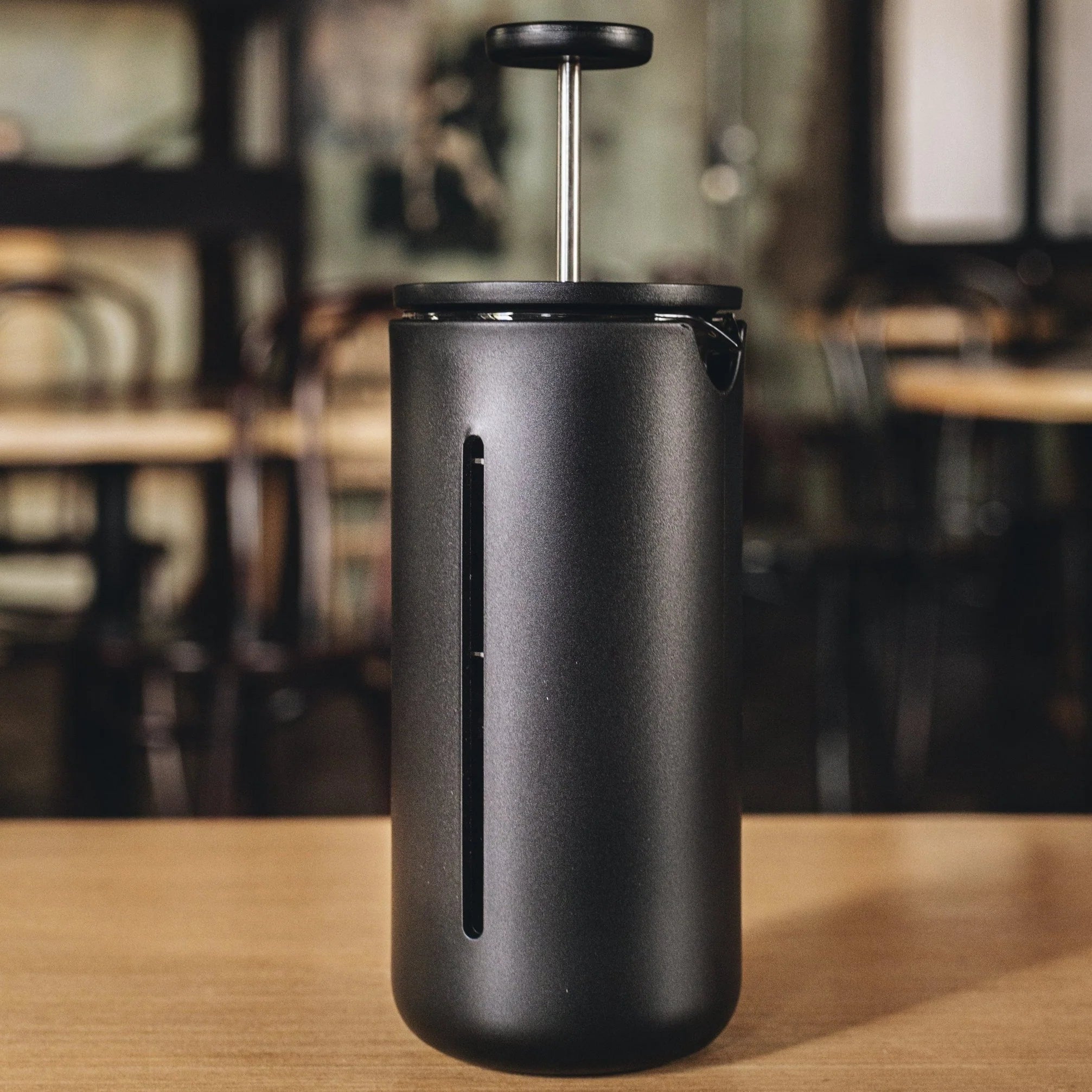 Black TIMEMORE U French Press coffee press on a wooden table with a blurred café background