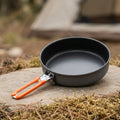 A FireMaple Camping pan with orange handles on a natural outdoor setting
