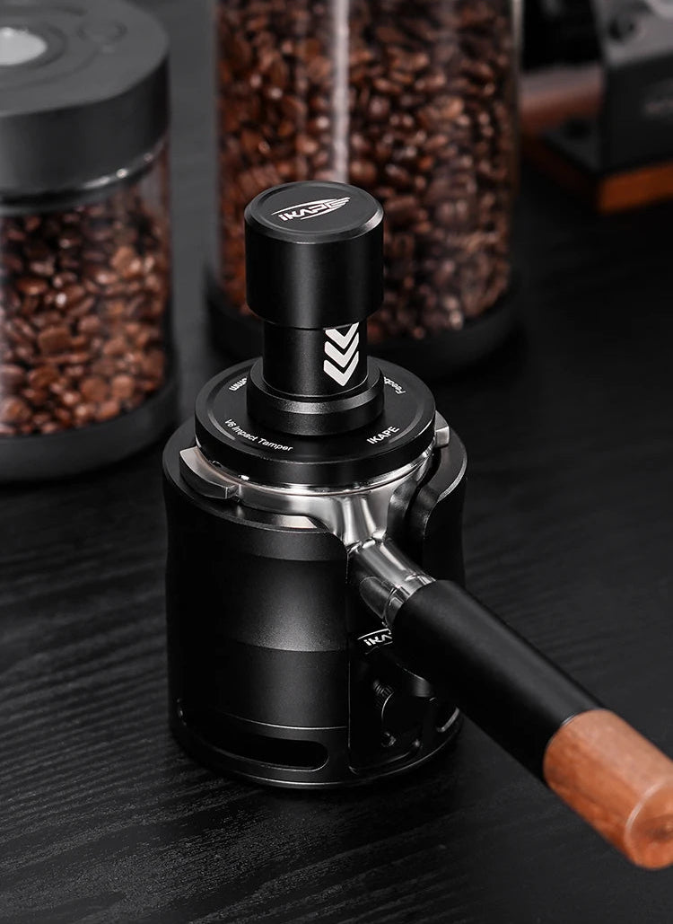 IKAPE tamper and black coffee grinder with wooden handle on a dark surface, surrounded by coffee beans.