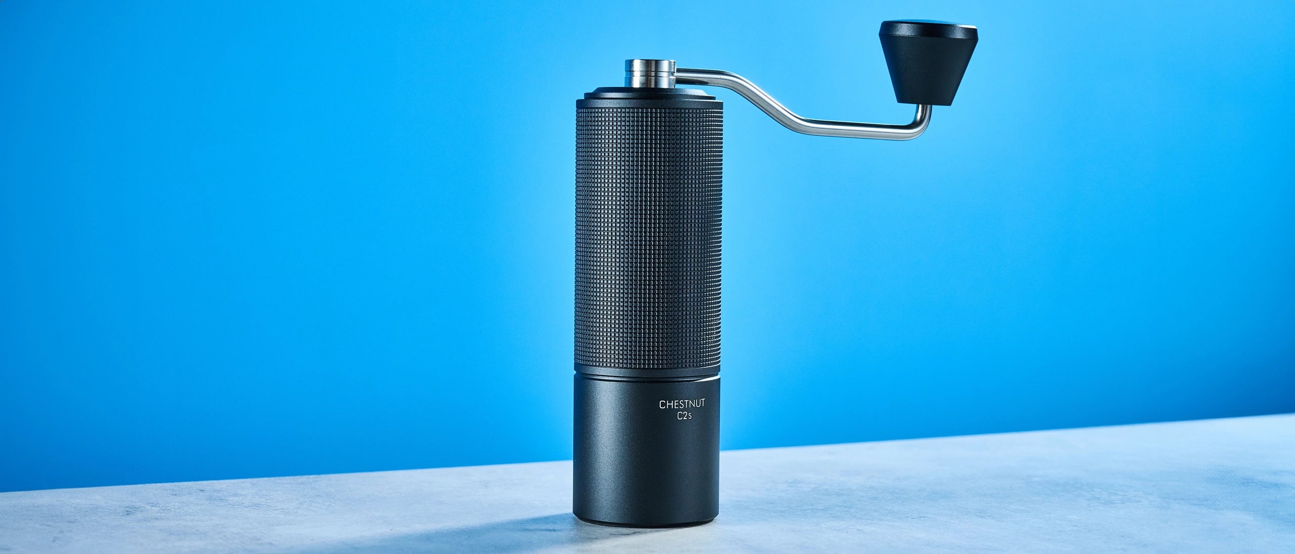 Studio shot of a TIMEMORE manual coffee grinder featuring a blue background. 