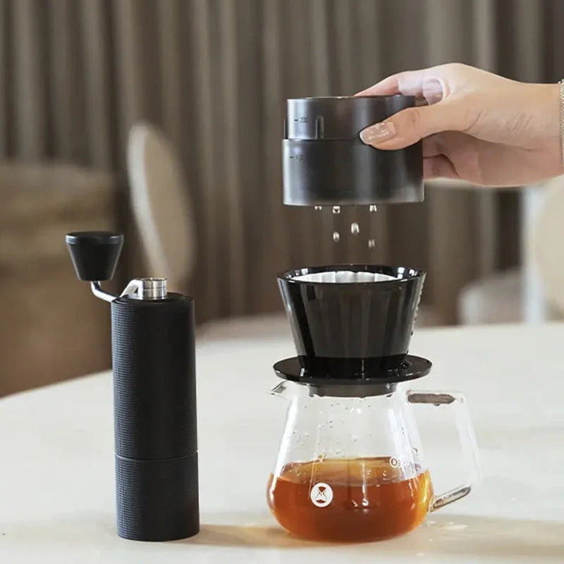 Hand holding a TIMEMORE Simple drip over a glass of brewed coffee on a table.